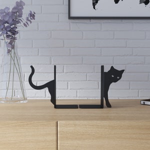 May include: Black metal bookends shaped like cats peeking around a corner. The bookends are a decorative way to hold books upright on a shelf.