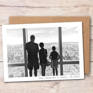 May include: A black and white photograph printed on a rectangular card, showing three figures from behind looking out a large window at a city skyline. The text "The Johnsons @ Dubai, 05.2006" is printed in the bottom right corner of the white border.