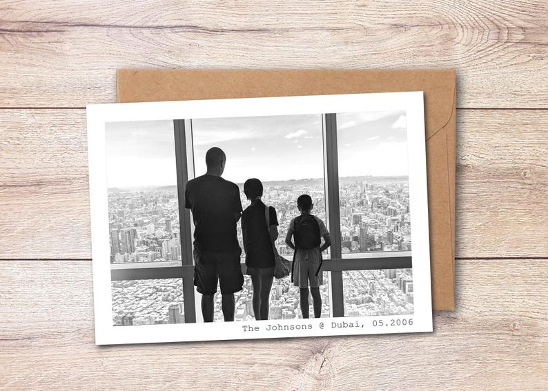 May include: A black and white photograph printed on a rectangular card, showing three figures from behind looking out a large window at a city skyline. The text "The Johnsons @ Dubai, 05.2006" is printed in the bottom right corner of the white border.