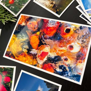 May include: A rectangular photographic print featuring a vibrant, high-angle view of multiple koi fish swimming in water. The fish display bright orange, white, and black patterns, with light reflecting off the rippling water surface, creating a dynamic scene.