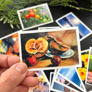 May include: A rectangular art print featuring a colored pencil drawing of a sliced yellow and orange fruit, a whole dark fruit on a small plate, and two small round red fruits arranged on a surface with a warm, textured brown background.