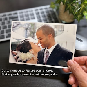 May include: A rectangular photograph showing a person with dark hair wearing a white floral hair accessory and a person in a dark suit with a white shirt and striped tie. The text reads: Custom-made to feature your photos. Making each moment a unique keepsake.