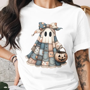 Könnte beinhalten: Weißes T-Shirt mit einer Illustration eines Geistes in einem Patchwork-Kostüm, der einen Kürbis-Eimer hält. Der Geist hat eine florale Schleife und einen freundlichen Ausdruck. Das Design ist in Pastellfarben gehalten, ideal für Halloween.