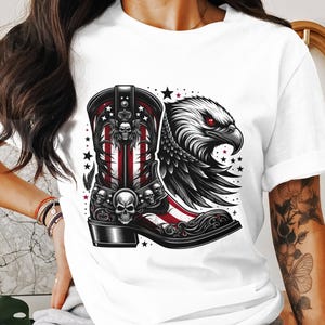May include: White t-shirt featuring a detailed graphic of a cowboy boot with a skull design, American flag stripes, and an eagle head with red eyes. The design incorporates stars and a decorative border.