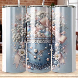 May include: A light blue tumbler with a floral and pearl design. The design includes a denim pocket with lace trim, white daisies, pink bows, and various sized pearls. The tumbler has a silver straw.