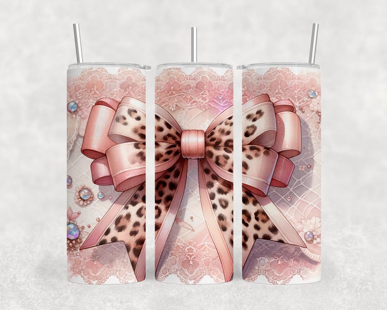 May include: A set of three stainless steel tumblers with a pink bow design. The bow features a leopard print center and pink ribbons. The background has a lace pattern with decorative jewels and a silver straw.