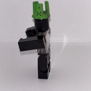May include: A black and clear plastic toy figure with a green crown. The figure has a black head and body, with clear plastic for the torso and legs. The green crown has several holes.