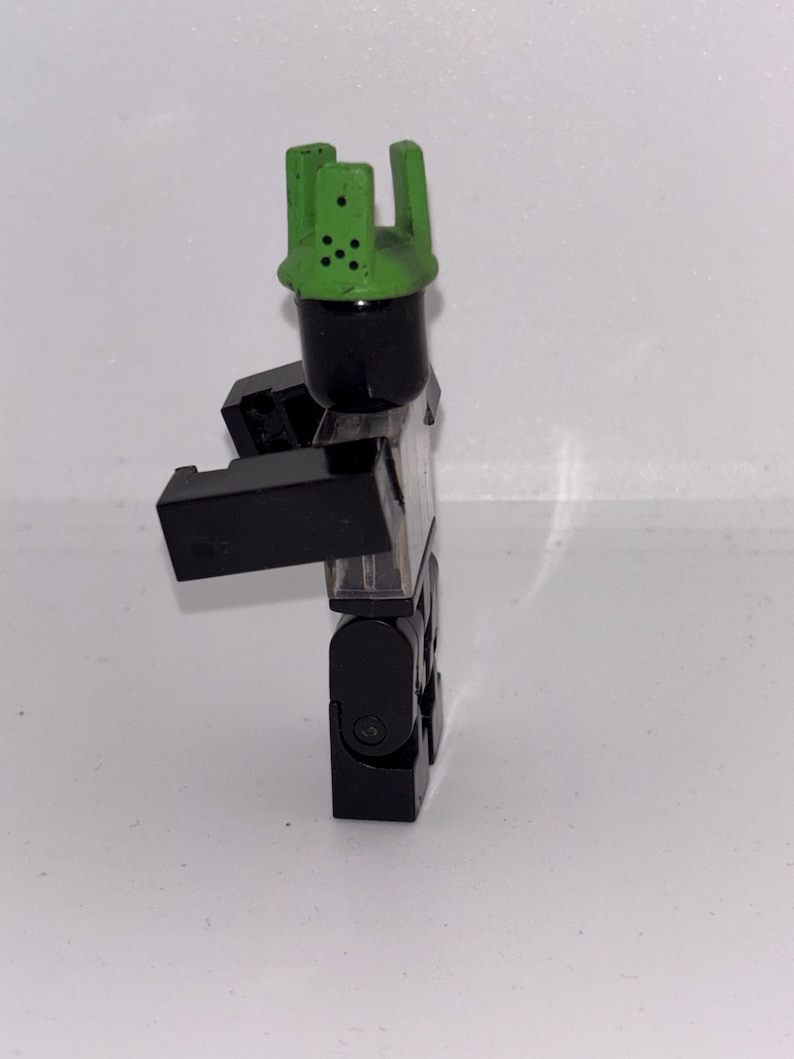 May include: A black and clear plastic toy figure with a green crown. The figure has a black head and body, with clear plastic for the torso and legs. The green crown has several holes.