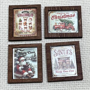 May include: Four miniature square wall signs with dark brown wooden frames. The signs feature vintage-style Christmas illustrations including a gingerbread bakery, a red truck with a tree, Santa Claus reading a book, and a Santa's workshop storefront.