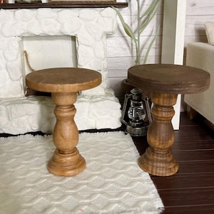 May include: Two wooden pedestal tables with a brown finish. The tables have a round top and a single, turned pedestal base.