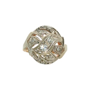 May include: A silver-toned metal ring featuring an intricate, swirling openwork design. The centerpiece is adorned with two prominent round-cut clear stones set vertically, surrounded by smaller accent stones embedded within the textured metal frame.