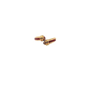 May include: A pair of gold-toned cufflinks with a rectangular design. Each cufflink features a row of small, rectangular red stones. The cufflinks are set against a white background.
