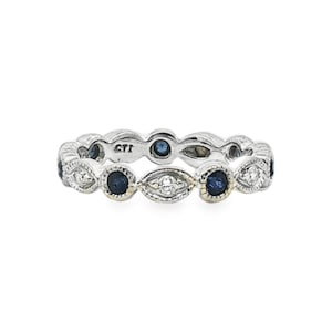 May include: A silver-toned band ring featuring an alternating pattern of round dark blue sapphires and marquise-shaped clear diamonds. The metal setting displays a textured milgrain edge detail throughout the band, with the letters CTI engraved inside.