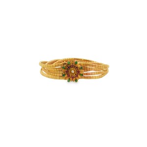 May include: Gold-toned bracelet with a floral centerpiece. The centerpiece features a central diamond surrounded by red and green gemstones. The bracelet has multiple strands of rectangular links.