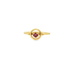 May include: A gold ring featuring a circular design with a vibrant red gemstone at the center. The ring's band has a textured appearance, and the gemstone is set within a smaller, inner circle.