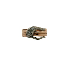 May include: A gold-toned ring with a snake design. The snake's head is dark gray with two clear stones. The ring has three bands of gold-colored metal. The snake's tail curves around the ring.