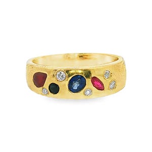 May include: A gold band ring with a textured finish, featuring an assortment of inlaid gemstones including round white diamonds, a large oval blue sapphire, a marquise-cut red ruby, and additional small round red and dark blue colored stones.