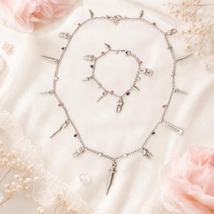 Può includere: Un set composto da collana e bracciale con ciondoli argentati a tema dentale, tra cui denti, uno spazzolino, una siringa e un tubetto con la scritta toothpaste, arricchito da piccole perline rosse e nere lungo le delicate catene metalliche.
