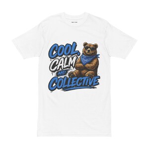 May include: A white short-sleeve t-shirt featuring a graphic of a brown bear wearing sunglasses and a blue bandana. The bear has its arms crossed. The text "COOL, CALM AND COLLECTIVE" is printed in blue and white lettering next to the bear illustration.