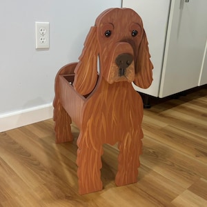 May include: A wooden dog-shaped planter painted in shades of brown. The planter features a detailed head, long ears, and a rectangular body for holding plants. The dog's legs are carved, and the overall design is rustic and charming.