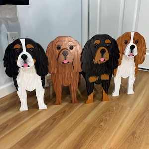 Peut inclure: Quatre figurines de chiens en bois autoportantes alignées. Le premier est noir, blanc et feu ; le deuxième est brun uni ; le troisième est noir et feu ; et le quatrième est brun et blanc. Chaque chien présente une texture de fourrure sculptée.