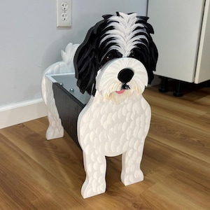 May include: A wooden dog-shaped planter painted in white, black, and pink. The dog planter has a black and white head, a black interior, and a white body. The planter is designed to hold plants and is a decorative item.