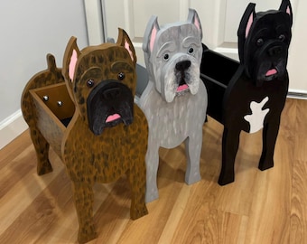 May include: Three wooden dog-shaped planters featuring a brindle, a gray, and a black dog. Each planter has a hollow center for holding items, with painted details including pink ears, black noses, and expressive eyes on each canine figure.