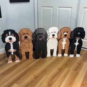Peut inclure: Une collection de six silhouettes de chiens en bois debout présentant diverses couleurs et motifs de pelage. Les figurines incluent un chien noir, blanc et beige, un chien brun clair uni, un chien gris foncé uni, un chien blanc uni, un chien brun clair et blanc, et un chien noir et blanc.