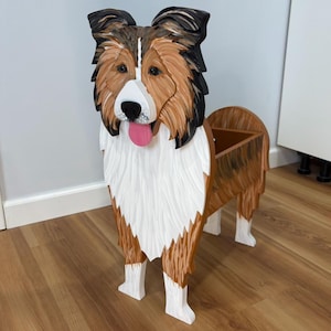 May include: A wooden dog-shaped planter, painted in shades of brown, white, and black. The dog has a pink tongue and a planter box on its back. The dog is standing on four white legs.
