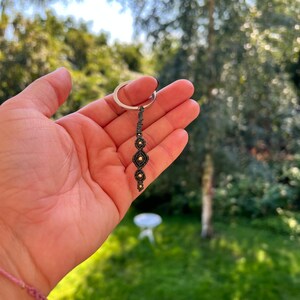Peut inclure: Un porte-clés noir et or avec une série de formes de diamants noués.