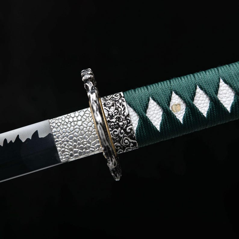 May include: Close-up of a katana sword. The blade is black and silver, with a detailed silver hilt and a green and white handle. The handle is wrapped in green fabric with white diamond-shaped accents. The hilt features intricate carvings.