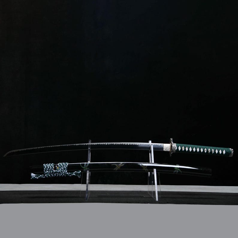 May include: A Japanese katana sword with a curved, black blade and a green handle with white diamond-shaped accents. The sword rests on a clear acrylic stand, with the scabbard below. The background is a solid black.