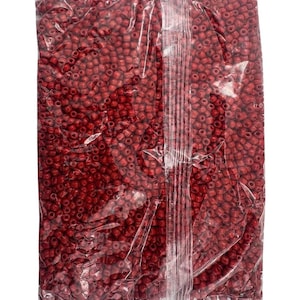 May include: A close-up view of a bag filled with small, red, round beads. The beads are packed tightly together and are visible through the clear plastic bag.