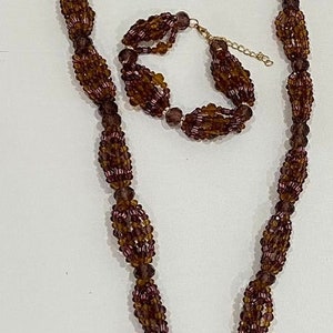 May include: A brown and purple beaded necklace with a tassel and a matching bracelet. The necklace is made of multiple strands of beads and has a long tassel at the end.