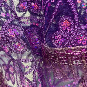 May include: Purple and iridescent sequined fabric with a fringe trim. The fabric is sheer and has a delicate floral pattern.