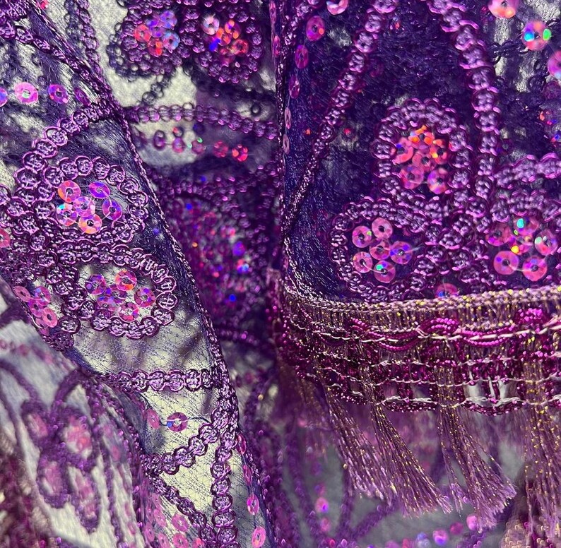 May include: Purple and iridescent sequined fabric with a fringe trim. The fabric is sheer and has a delicate floral pattern.