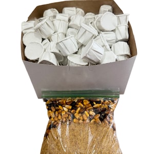 May include: A brown cardboard box filled with white paper cups, with a clear plastic bag containing yellow and brown corn kernels and a brown powder below the kernels.