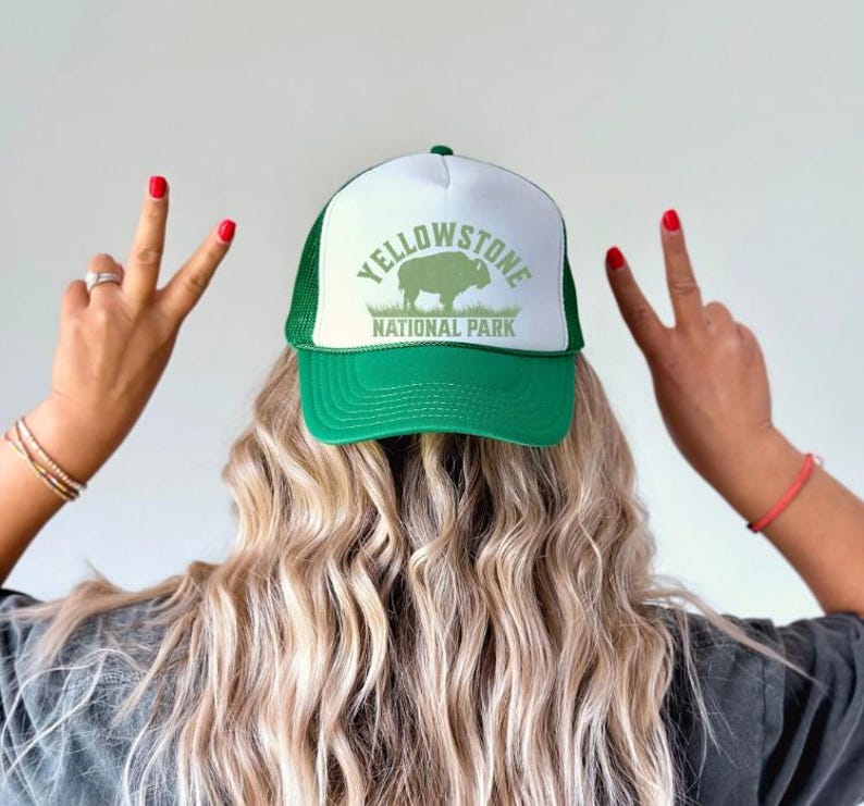 May include: A green and white trucker hat with a green mesh back. The hat has a white front panel with the text "Yellowstone National Park" in green letters and a silhouette of a bison in green.
