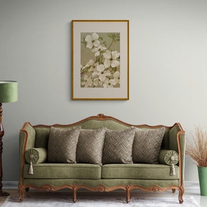 Może przedstawiać: Zielona welurowa sofa z rzeźbioną drewnianą ramą i czterema nogami. Sofa ma cztery poduszki z geometrycznym wzorem i obraz z kwiatami nad nią.