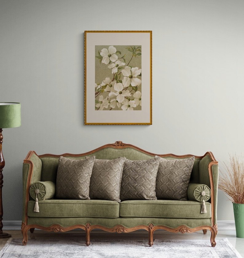 Może przedstawiać: Zielona welurowa sofa z rzeźbioną drewnianą ramą i czterema nogami. Sofa ma cztery poduszki z geometrycznym wzorem i obraz z kwiatami nad nią.