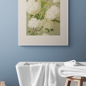 May include: A framed botanical illustration of white hydrangea flowers with green leaves on a light green background. The frame is white and the background is a light blue wall.