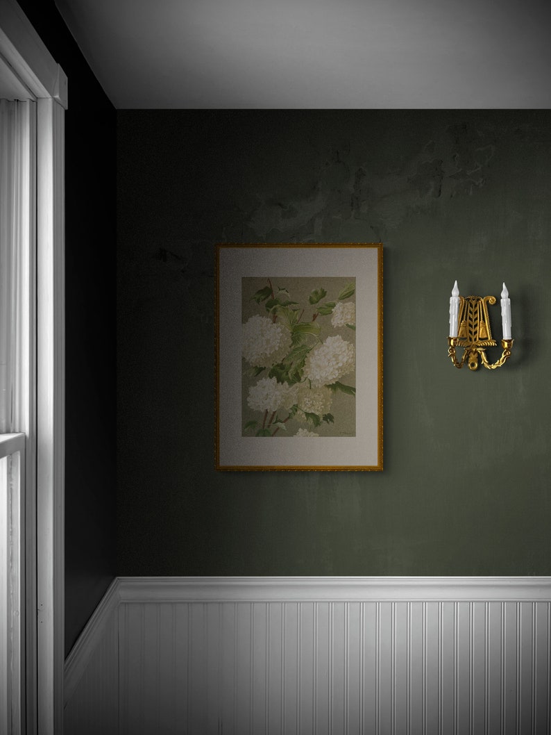 May include: A framed botanical print of white flowers with green leaves hangs on a dark green wall. A gold wall sconce with two candles is on the right side of the frame.