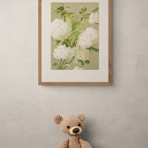 May include: A framed botanical illustration of white flowers with green leaves on a light green background. A crocheted teddy bear sits on a wooden table with a brown mug, coffee beans, and fall leaves.