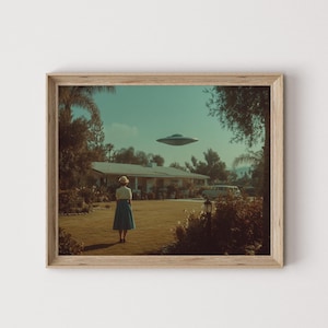 Puede incluir: Impresión enmarcada que representa a una mujer con falda y blusa en un jardín, mirando un OVNI sobre una casa. La obra de arte tiene una estética vintage, en tonos sepia, con un marco de madera marrón claro. La escena evoca misterio.