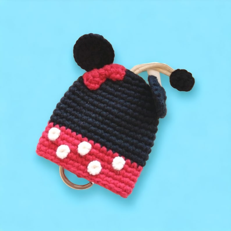 May include: A black and red crocheted key chain with white polka dots and Mickey Mouse ears. The keychain has a silver ring.