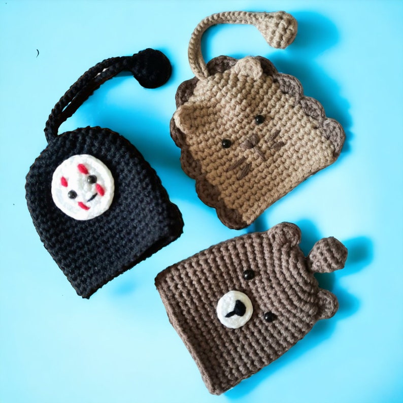May include: Three crocheted animal-shaped cup cozies. A black and white No Face character, a brown bear, and a brown cat.