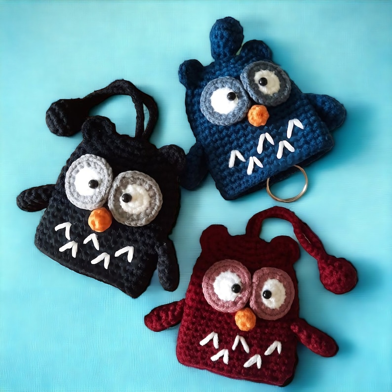 May include: Three crocheted owl keychains in blue, black, and burgundy. Each owl has white eyes, a small orange beak, and white stitching around the eyes.