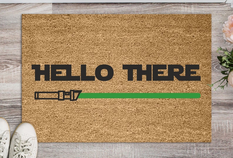 May include: A brown doormat with the text "HELLO THERE" in black letters and a green lightsaber graphic.