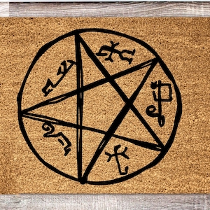 May include: A rectangular doormat with a light brown, textured surface. A black pentagram design with symbols is centered on the mat. The design is enclosed in a circle. The doormat is likely made of coir.