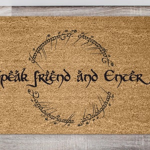 Puede incluir: Una alfombra de coco marrón con las palabras "Speak friend and enter" en escritura negra. Las palabras están rodeadas por un círculo de escritura élfica.